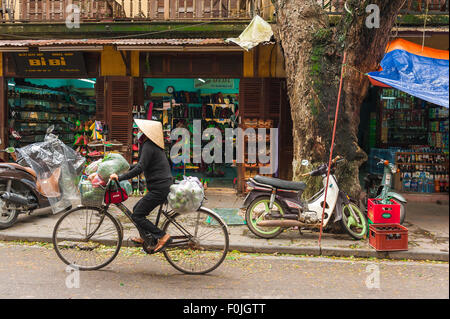 Il Vietnam donna bicicletta, una donna che indossa un cappello conico trasporta i sacchi di verdure sulla sua bicicletta in una strada di Hoi An, Vietnam centrale. Foto Stock