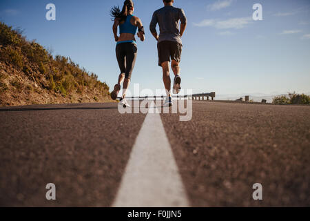 Vista posteriore di due giovani una formazione insieme sulla strada. L uomo e la donna sulla corsa mattutina sul giorno di estate. Bassa angolazione del giovane jo Foto Stock