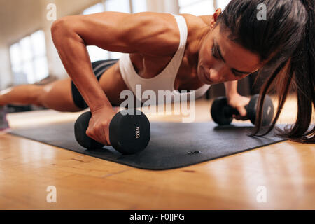 Forte giovane donna facendo spingere ups esercizio con manubri. Modello di fitness facendo un allenamento intenso in palestra. Foto Stock