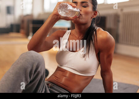 Donna Fitness acqua potabile dalla bottiglia. Muscolare di giovani donne presso la palestra prendendo una pausa da allenamento. Foto Stock