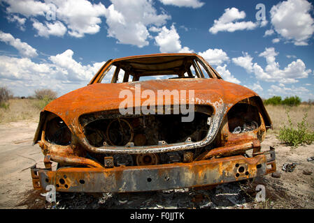 Un ampio angolo di visione di un vecchio arrugginito auto abbandonate sotto puffy blue skies nel gioco Riserva del Kalahari centrale in Botswana Foto Stock