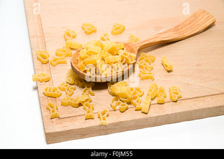 La pasta in forma di animali e un cucchiaio di legno su sfondo bianco Foto Stock