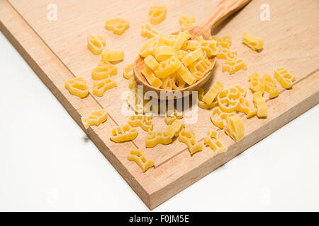 La pasta in forma di animali e un cucchiaio di legno su sfondo bianco Foto Stock