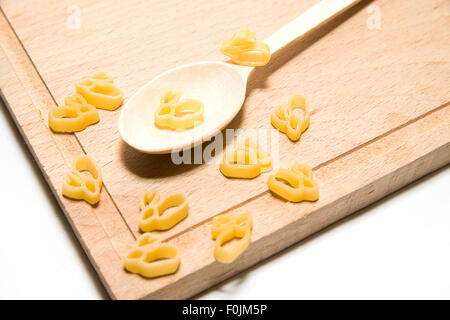 La pasta in forma di animali e un cucchiaio di legno su sfondo bianco Foto Stock