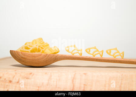 La pasta in forma di animali e un cucchiaio di legno su sfondo bianco Foto Stock