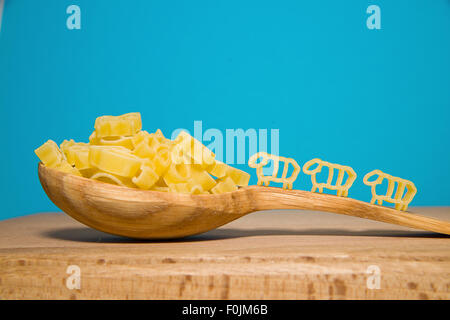 La pasta in forma di animali e un cucchiaio di legno su uno sfondo blu Foto Stock