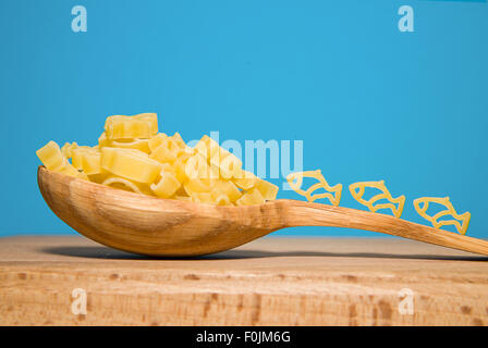 La pasta in forma di animali e un cucchiaio di legno su uno sfondo blu Foto Stock