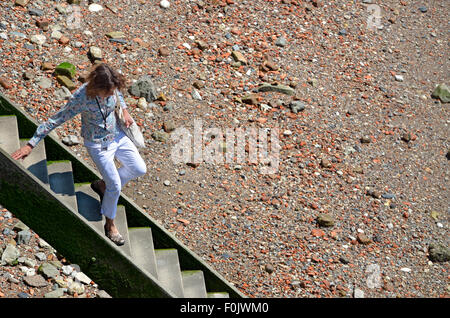 Londra, Inghilterra, Regno Unito. Donna scendendo di gradini di pietra al Tamigi a bassa marea, vicino al Millennium Bridge Foto Stock