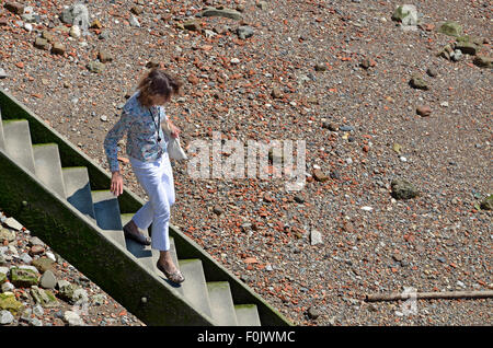 Londra, Inghilterra, Regno Unito. Donna scendendo di gradini di pietra al Tamigi a bassa marea, vicino al Millennium Bridge Foto Stock