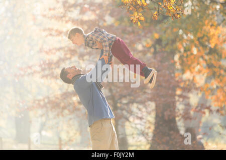 Padre figlio di sollevamento overhead nei boschi con foglie di autunno Foto Stock