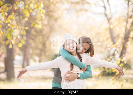 Ritratto madre abbracciando la figlia con le braccia aperte tra foglie di autunno Foto Stock