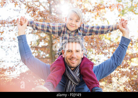 Ritratto sorridente padre figlio che porta sulle spalle sotto le foglie di autunno Foto Stock