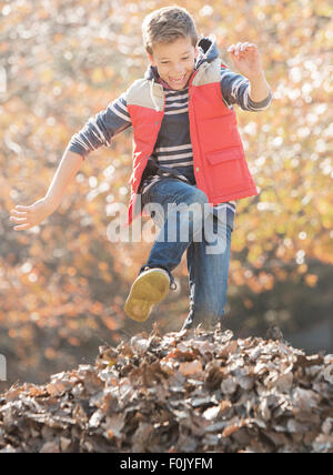 Ragazzo entusiasta saltando su mucchio di foglie di autunno Foto Stock