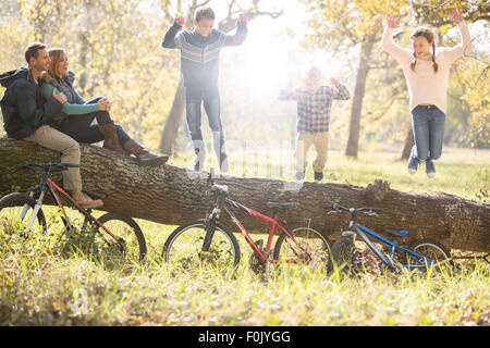 Famiglia giocando sul registro caduti con le biciclette nel bosco Foto Stock