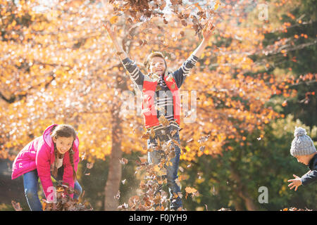 Giocoso ragazzi e una ragazza correre e saltare in foglie di autunno Foto Stock