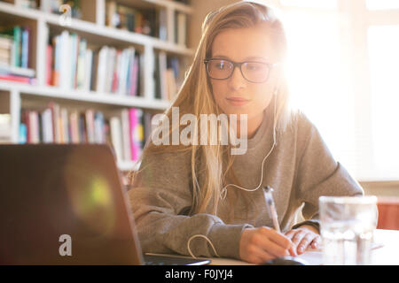 Ragazza adolescente con cuffie facendo compiti a casa con il computer portatile Foto Stock