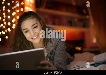 Sorridente ragazza adolescente utilizzando digitale compressa sul letto Foto Stock