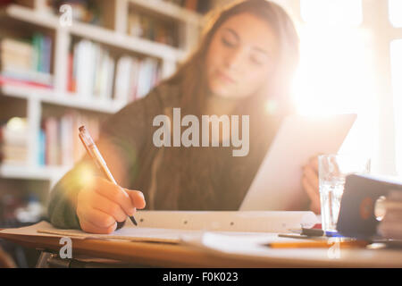 Ragazza adolescente con tavoletta digitale facendo compiti a sunny scrivania Foto Stock