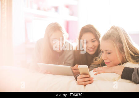 Le ragazze adolescenti tramite telefono cellulare e la tavoletta digitale nella soleggiata camera da letto Foto Stock