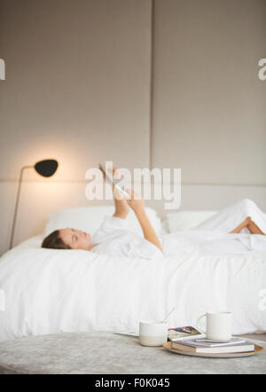 Donna in accappatoio posa sul letto tramite tavoletta digitale Foto Stock