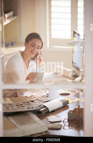 Interior designer esaminando campioni e parlando al cellulare in home office Foto Stock