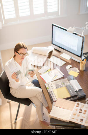 Interior designer esaminando campioni alla scrivania in ufficio in casa Foto Stock