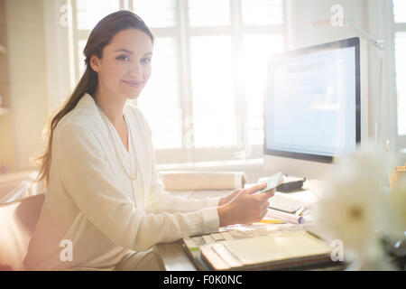 Ritratto sorridente interior designer con campioni a computer in ufficio in casa Foto Stock