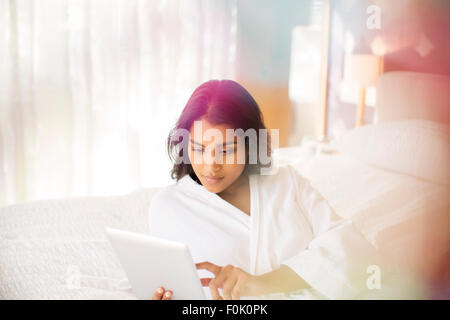 Donna in accappatoio con tavoletta digitale sul letto Foto Stock