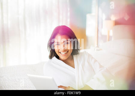 Ritratto di donna sorridente in accappatoio con tavoletta digitale sul letto Foto Stock