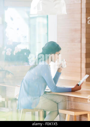 Donna di bere il caffè e con tavoletta digitale al bar per la prima colazione Foto Stock