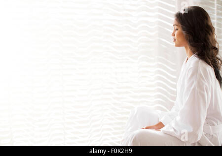 Serena donna in accappatoio meditando a finestra piena di sole Foto Stock