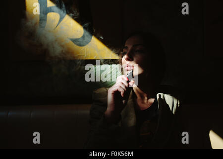 La ragazza si siede e fuma sigaretta elettronica Foto Stock