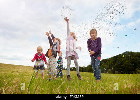 Cinque bambini piccoli gettando coriandoli su un prato Foto Stock