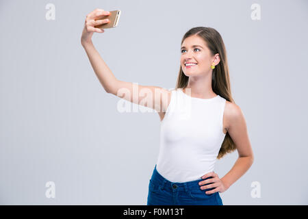 Ritratto di una donna sorridente adolescente rendendo selfie foto sullo smartphone isolato su uno sfondo bianco Foto Stock