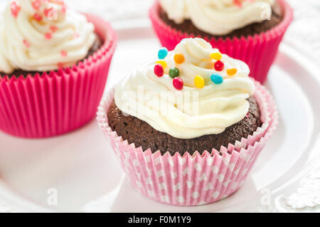 Fancy tortini di cioccolato con panna alla vaniglia e colorate glasse e decorazioni Foto Stock