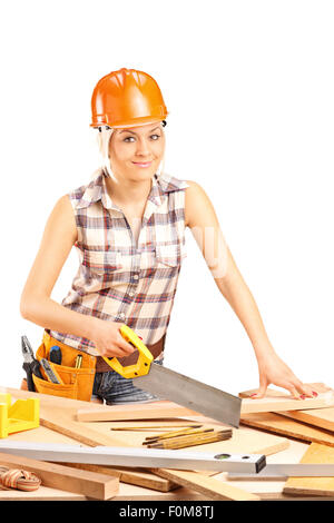 Colpo verticale di una femmina di falegname con un casco arancione il taglio di una trave di legno con un handsaw isolati su sfondo bianco Foto Stock