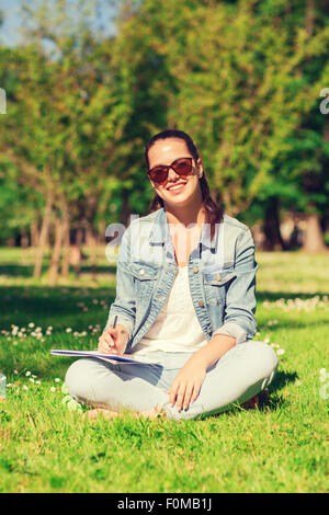 Sorridente ragazza giovane con la scrittura del notebook in posizione di parcheggio Foto Stock