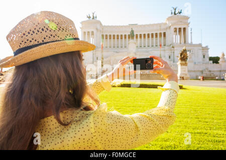 Visto da dietro una turista prende una foto della piazza Venezia monumento a distanza su un giorno d'estate a Roma. Foto Stock