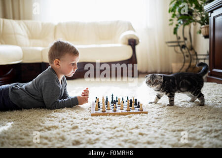 Little Boy gioca a scacchi sdraiato sul pavimento Foto Stock