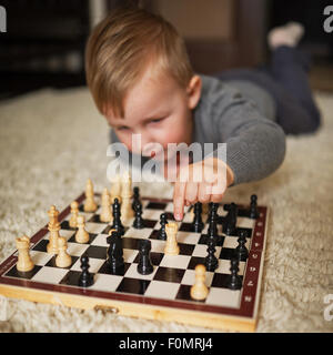 Little Boy gioca a scacchi sdraiato sul pavimento Foto Stock