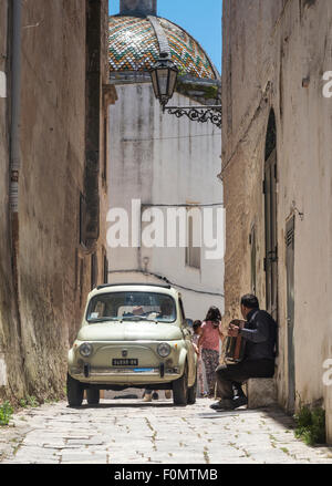 Un musicista di strada accordianist e una Fiat 500 soddisfare nei vicoli di Ostuni, Puglia, Italia Foto Stock