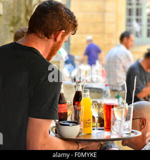Cameriere francese porta il vassoio pieno di bevande ai clienti presso il bar esterno tavoli in Place de l' Hotel de Ville Aix en Provence, nel sud della Francia Foto Stock