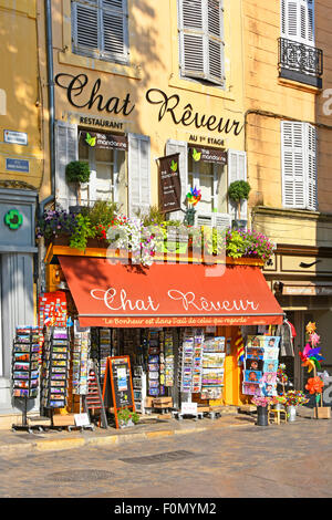 Shopfront con rack da cartolina sul marciapiede e ristorante sopra in un angolo della Place de l'Hotel de Ville in Aix en Provence Sud della Francia Foto Stock