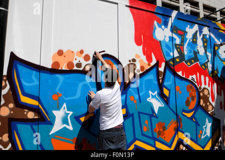 Uomo di verniciatura a spruzzo di graffiti su Great Eastern Street palizzata in Shoreditch, East London REGNO UNITO KATHY DEWITT Foto Stock