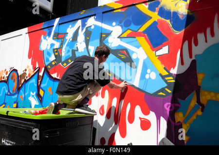 Uomo di verniciatura a spruzzo di graffiti su Great Eastern Street palizzata in Shoreditch, East London REGNO UNITO KATHY DEWITT Foto Stock