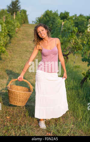 Attraente brunnette felice ragazza in vigna a lavorare sulla vendemmia con un grande cesto di vimini Foto Stock