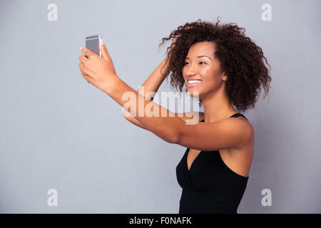 Ritratto di un sorridente afro american donna fare selfie foto sullo smartphone su sfondo grigio Foto Stock