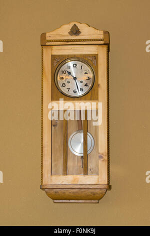 Un orologio in legno di stile tradizionale montato a parete interno con pendolo e una faccia con numeri in una casa in Austria. Concetto: Tempo Foto Stock