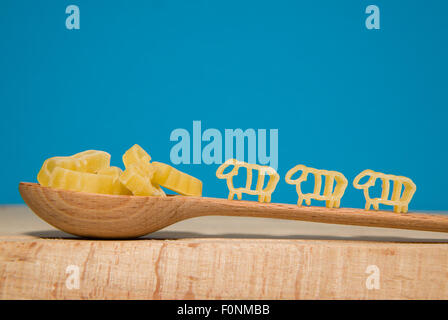 La pasta in forma di animali e un cucchiaio di legno su uno sfondo blu Foto Stock