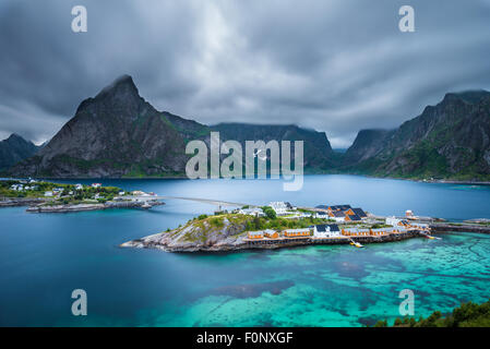 Montare Olstind sopra le cabine gialle e turquise acque di Sakrisoy nei villaggio di pescatori sulle isole Lofoten in Norvegia a sera bl Foto Stock